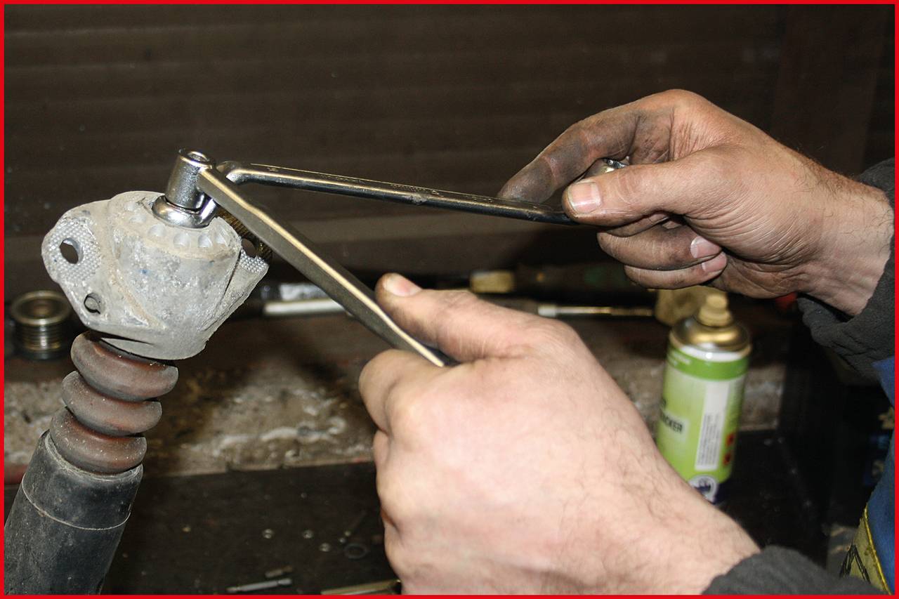 'Hands of a person repairing a car part, using two spanners, with a workbench and tools in the background.'