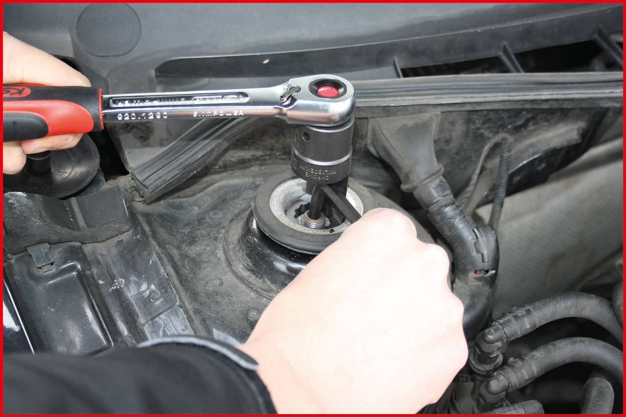 A person is tightening a screw in a car's engine bay using a ratchet tool.