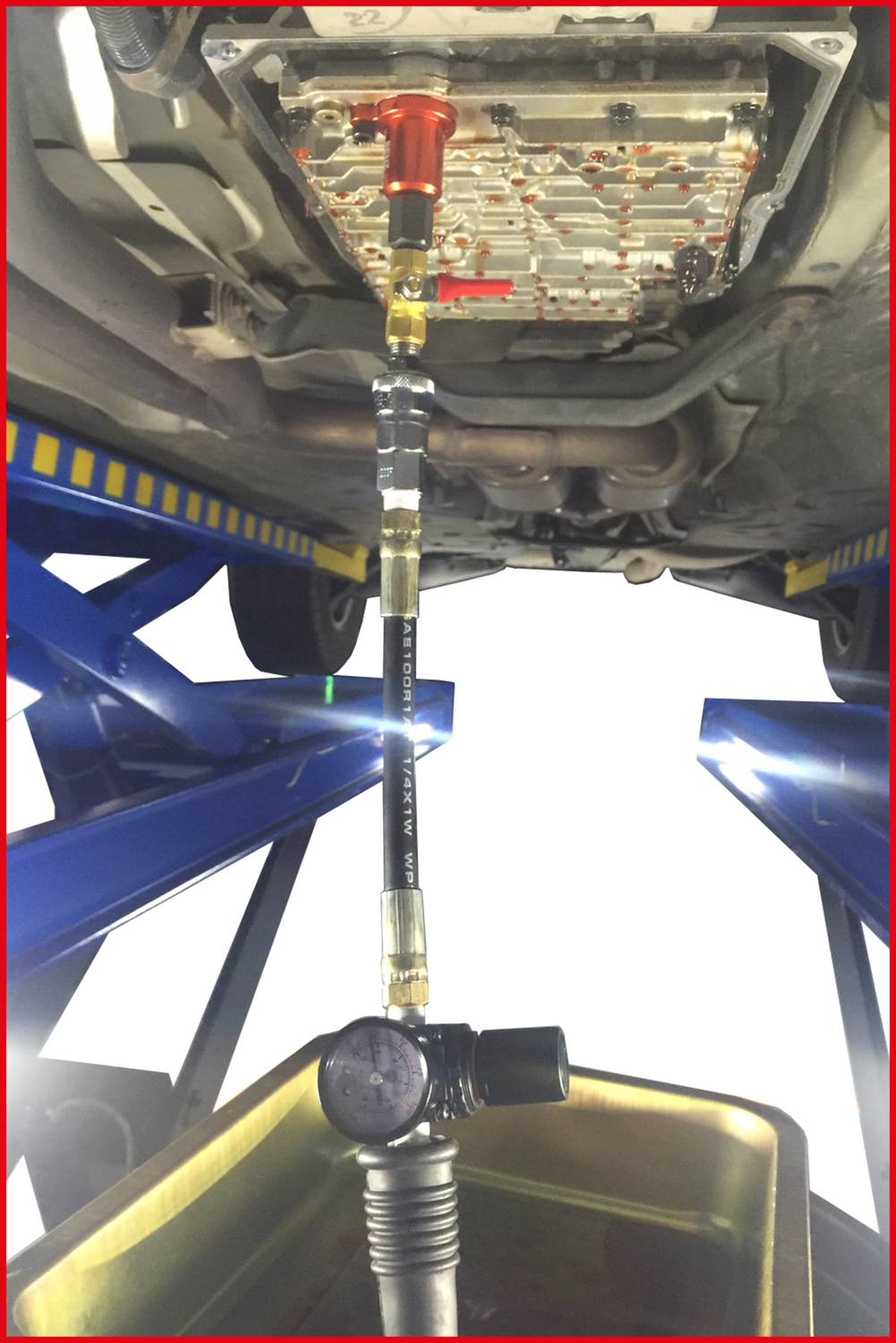 The car is positioned on a vehicle lift. Transmission oil is being drained through a hose into a yellow collection container.