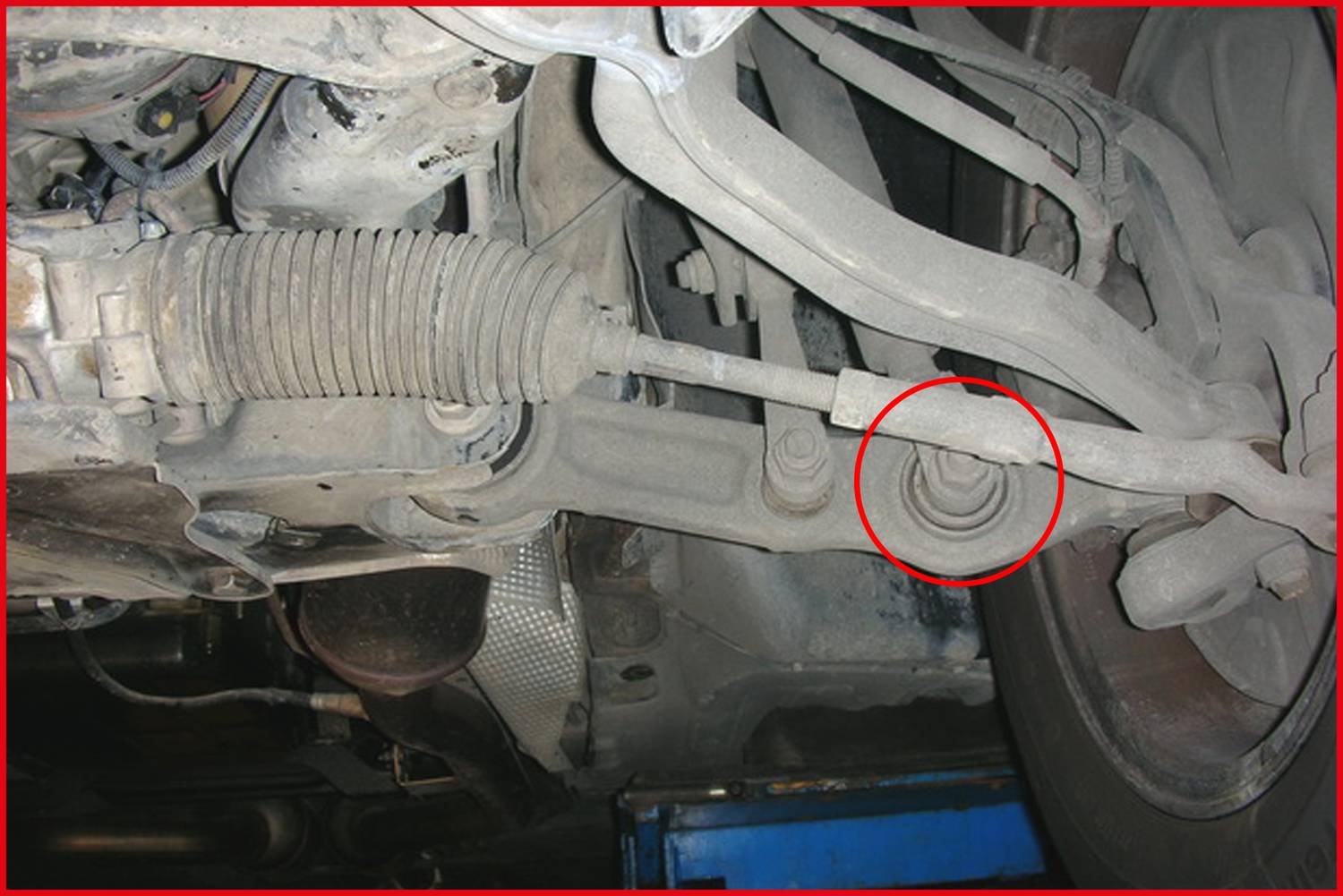 Underneath view of a car showing the chassis with focus on the damaged or loose track rod connection, circled in red.