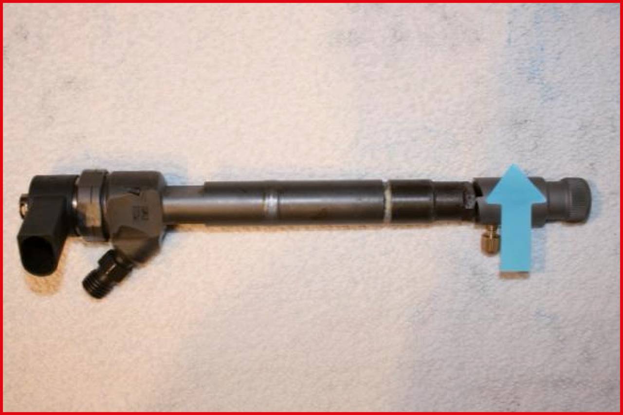 A metal pipe with black connecting pieces lies on a grey surface. A blue arrow points to the right end of the pipe.