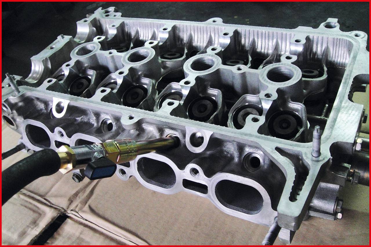 Metal cylinder head gasket on a table. A tool is attached to the cylinder head, apparently for processing or inspection.