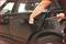 A person is attempting to break into the passenger door of a black car using a tool.