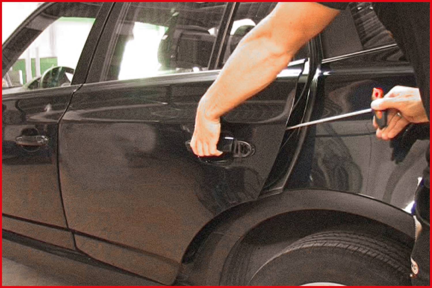 A person, whose face is obscured, is attempting to forcibly open a car at the driver's door using a screwdriver.