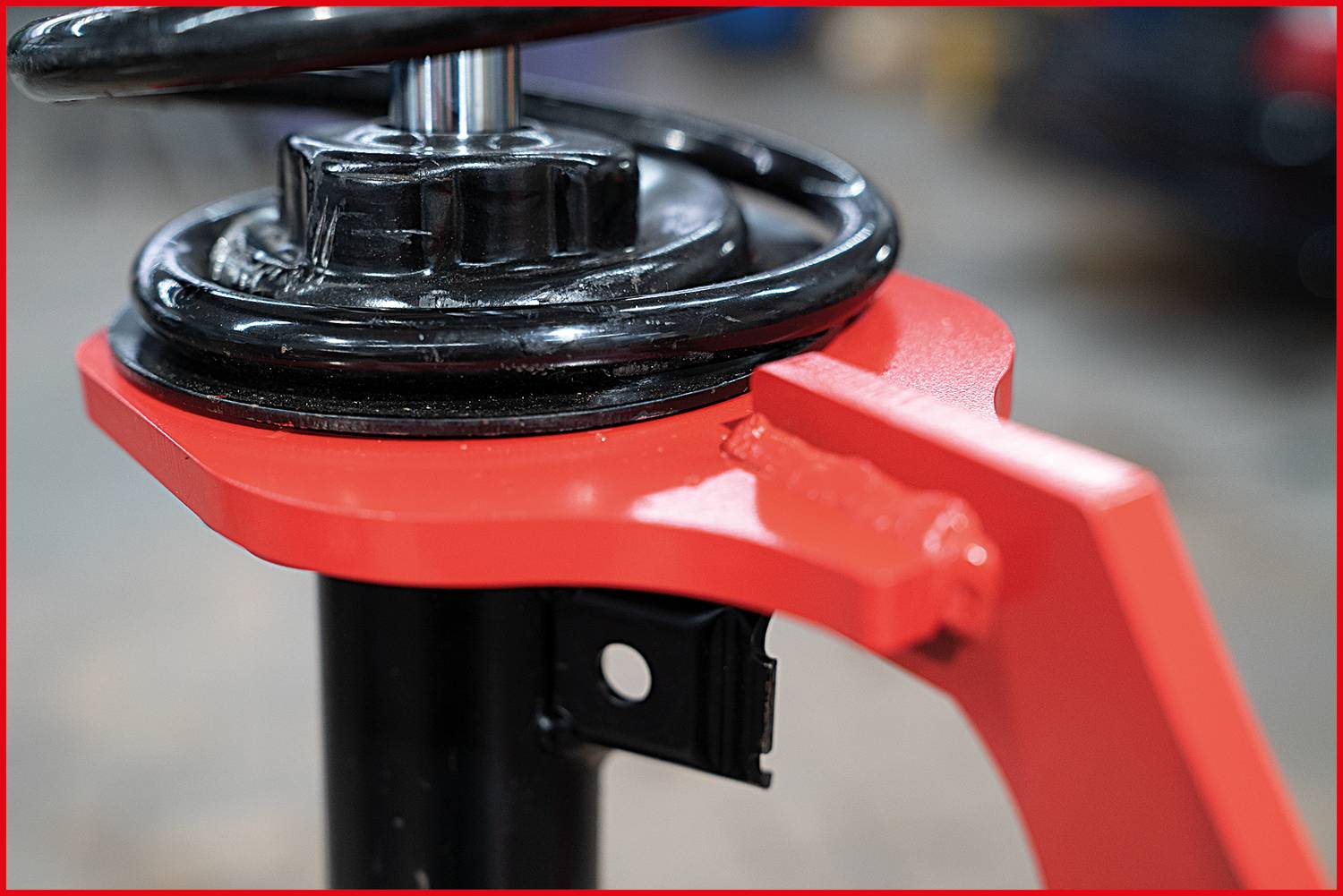 Close-up of a car shock absorber with a red mounting bracket. The shock absorber is partially assembled. Mechanical environment in the background.