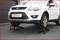 A white car is parked on two black vehicle ramps, which are lifting the vehicle. It is situated on a paved surface.