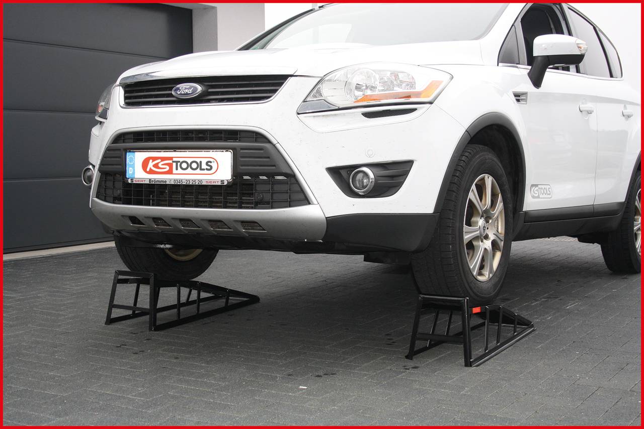 A white car is parked on black ramps, which are being used to lift the vehicle. A garage door can be seen in the background.