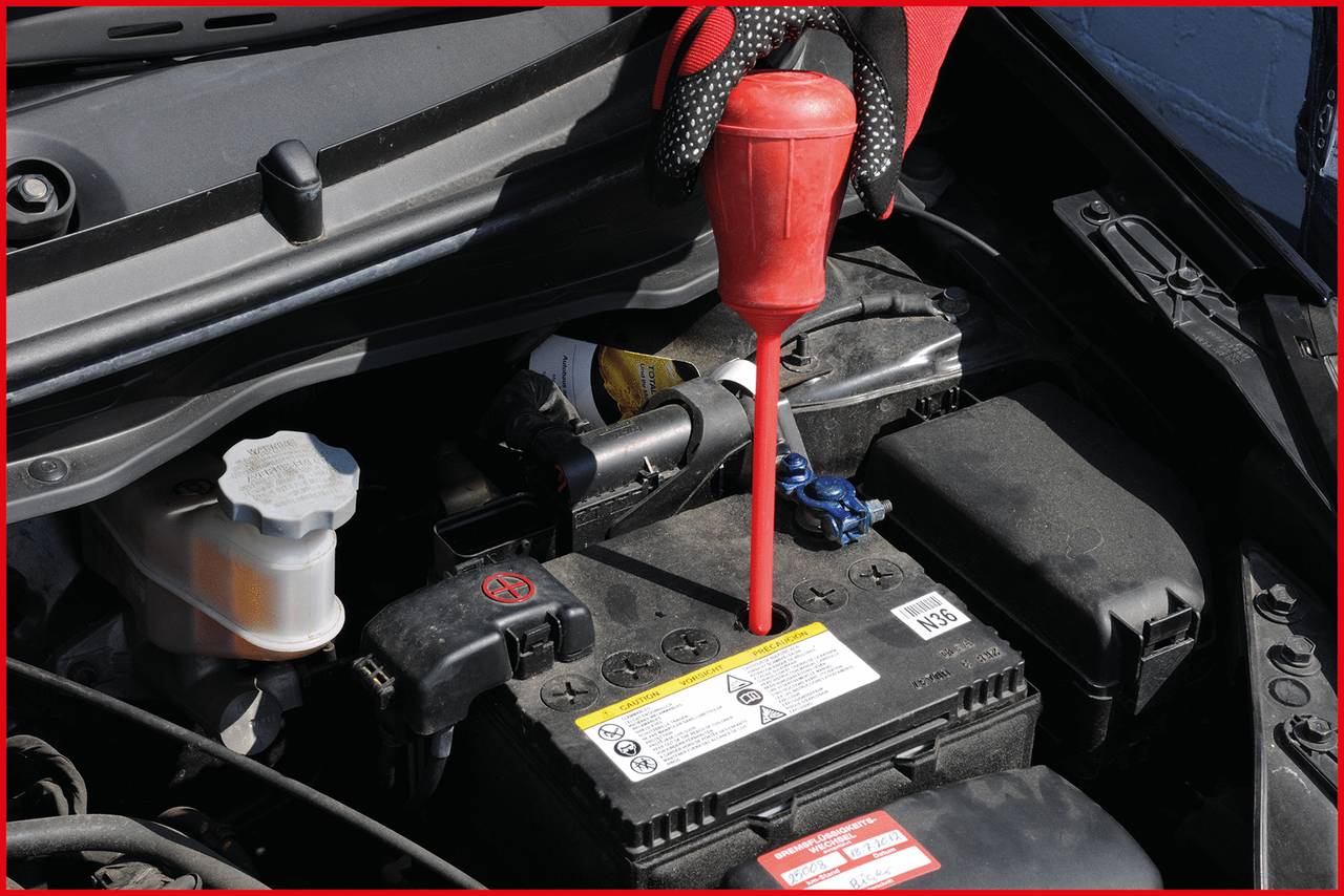 A person is checking the fluid level in a car battery with a dipstick in the engine compartment.