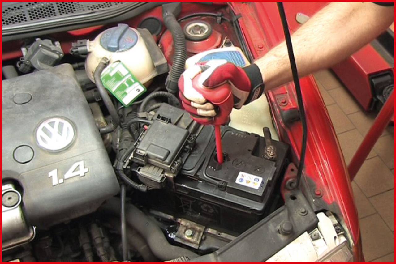 A mechanic is checking the charge level of a car battery with a measuring device in a car with the battery cover removed.