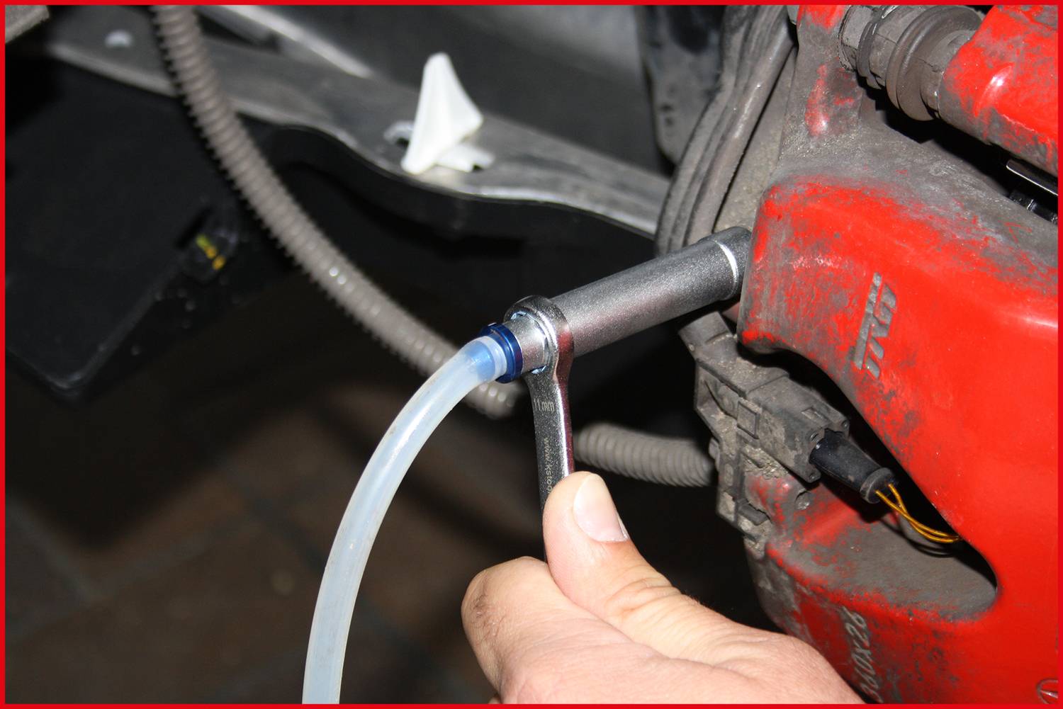 A person is using a brake bleeding device on a vehicle. A transparent tube is connected to a spanner.