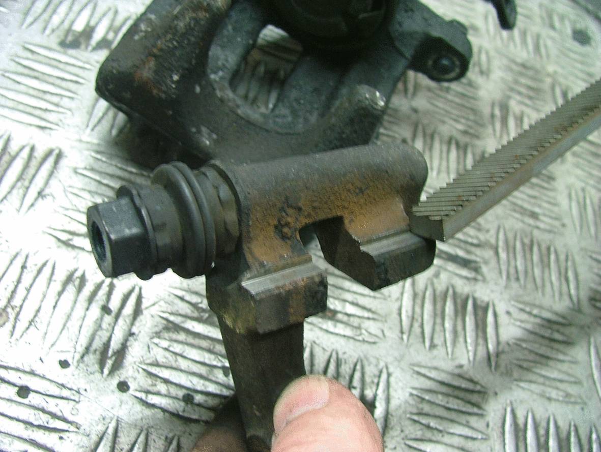 A close-up of a metallic car part on a textured surface. A tool is engaging with the part, potentially for repair.