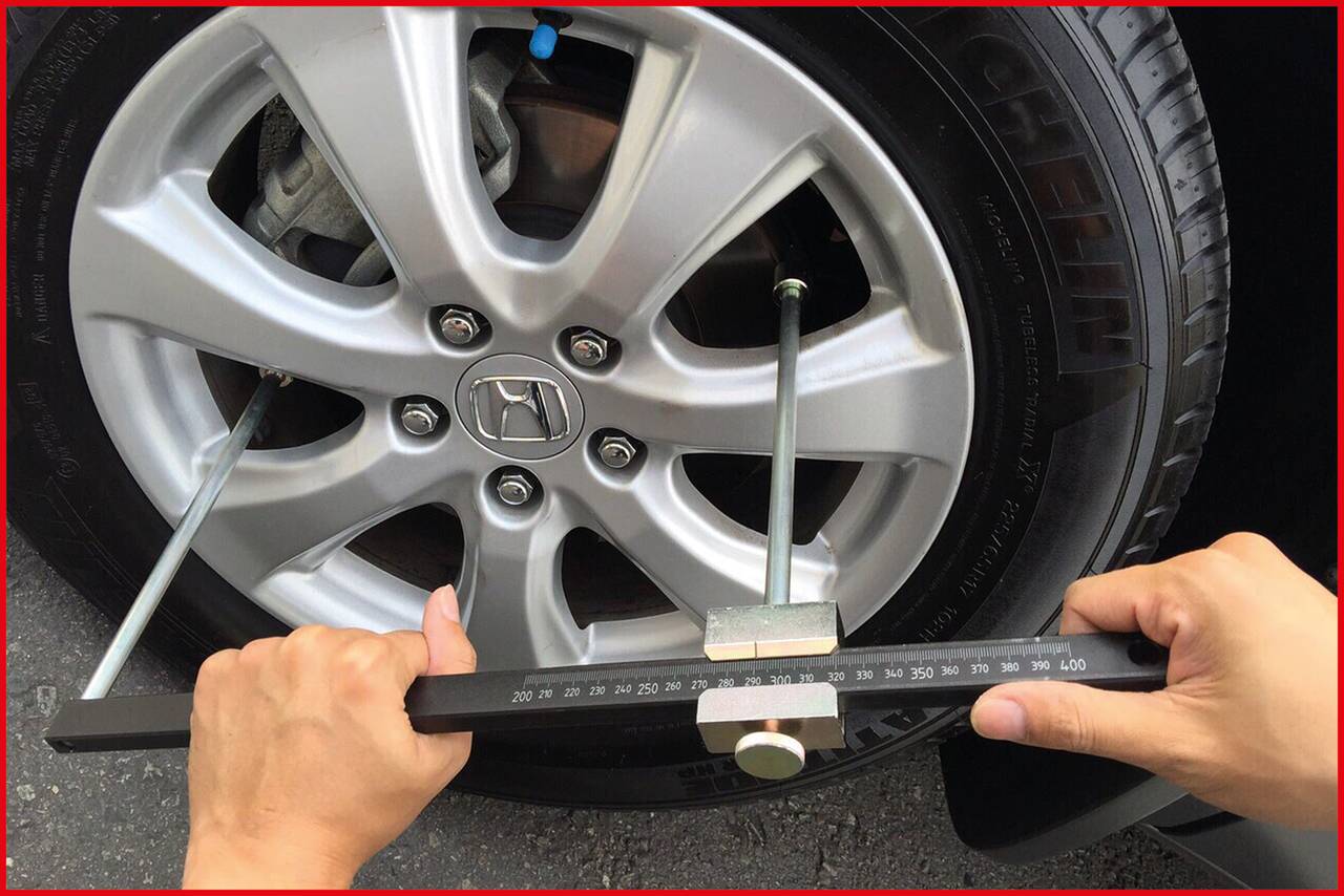 A person is measuring the diameter of a car tyre with a large calliper. The tyre is mounted on a silver wheel rim.