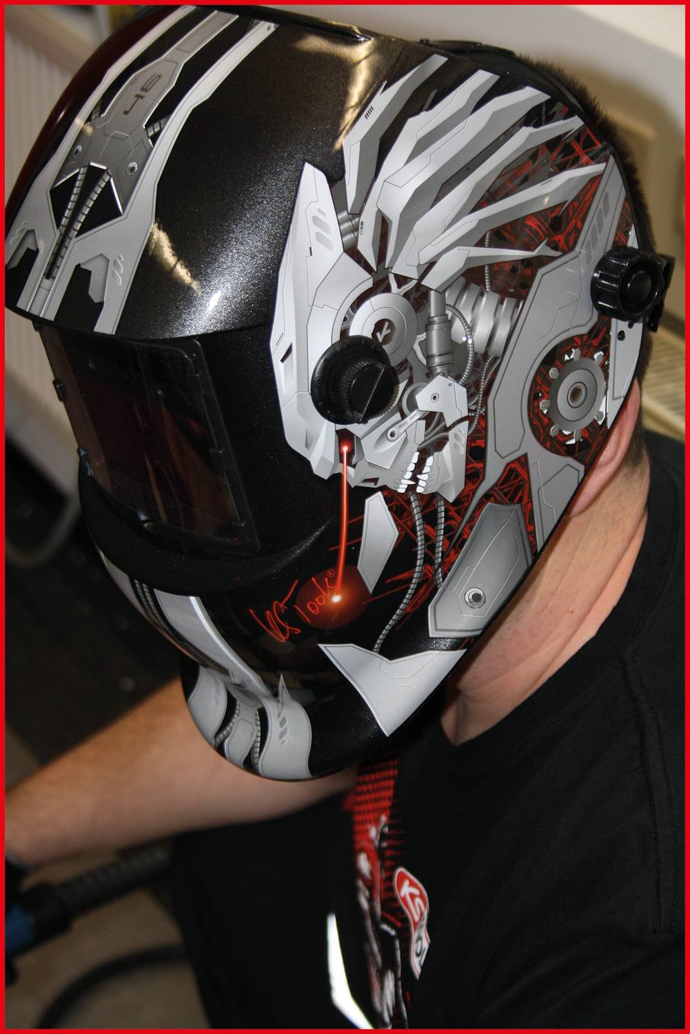 A welder wearing an artistically designed, modern helmet, revealing details of mechanical elements and a skull.