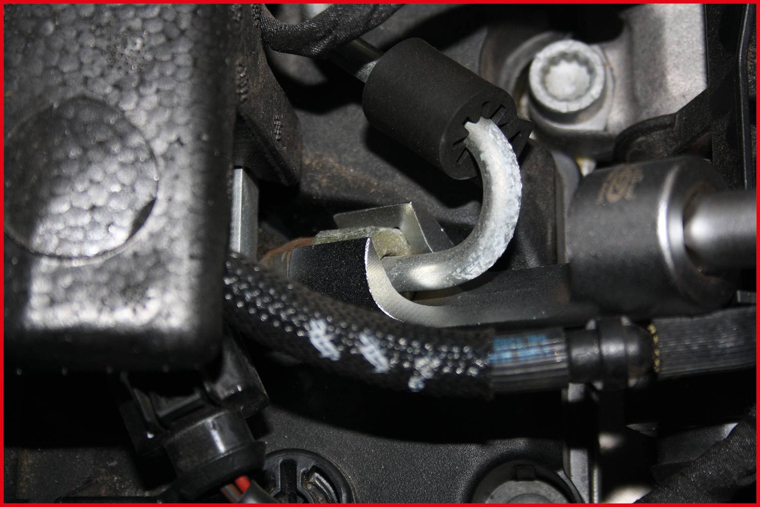 Close-up of an engine bay with various hoses, cables, and a metal pipe in a car.