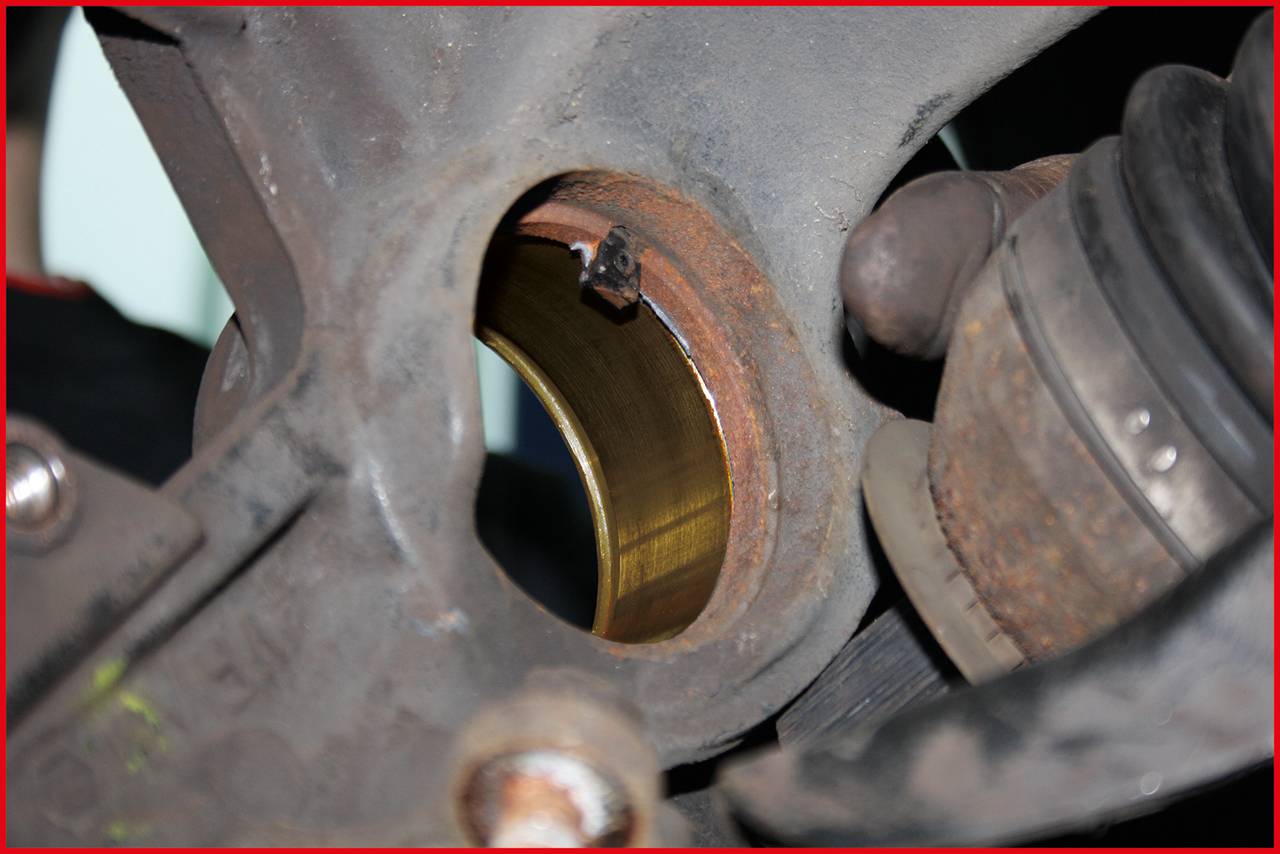 Close-up of a car component focusing on a round, metallic bearing in a suspension, with a gloved hand working on it.