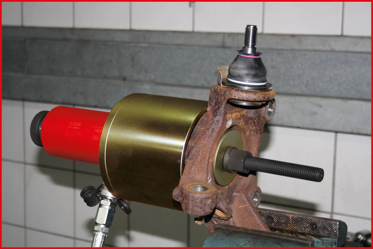 A tensioned wheel hub with a wheel bearing puller in a workshop environment, showing the assembly process.