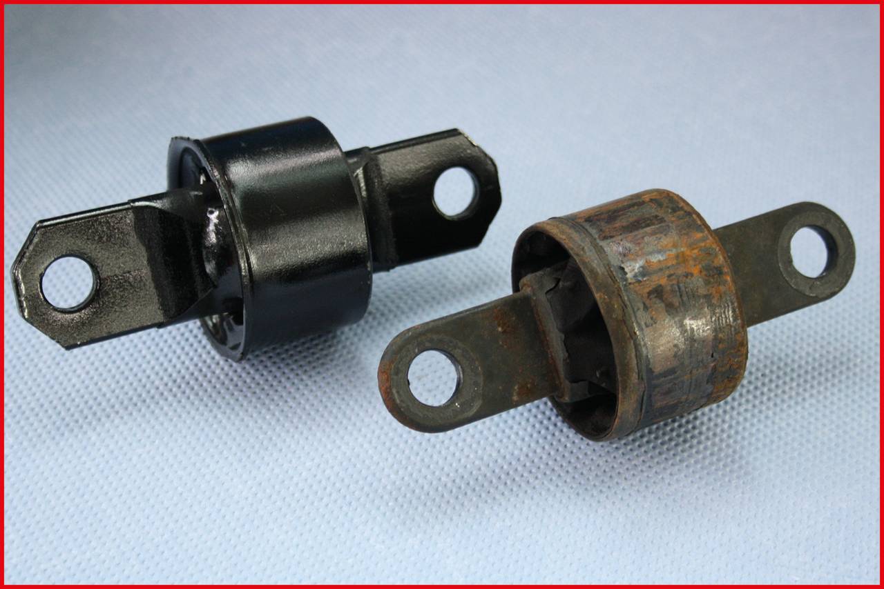 A new and an old car part lie side by side on a surface. The new part is black and shiny, the old one rusty and worn.