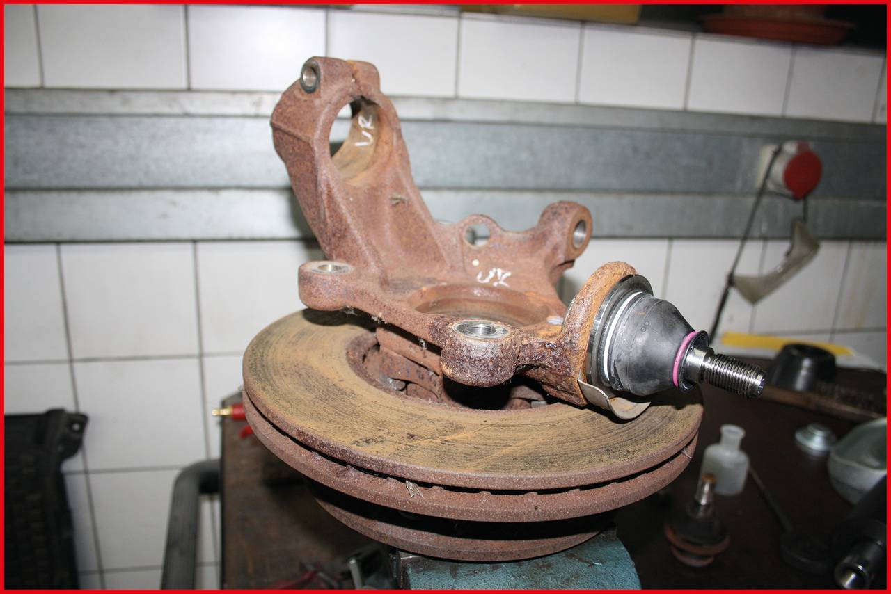 A rusty car part, presumably a brake calliper with brake disc, lies on a workbench in a workshop.