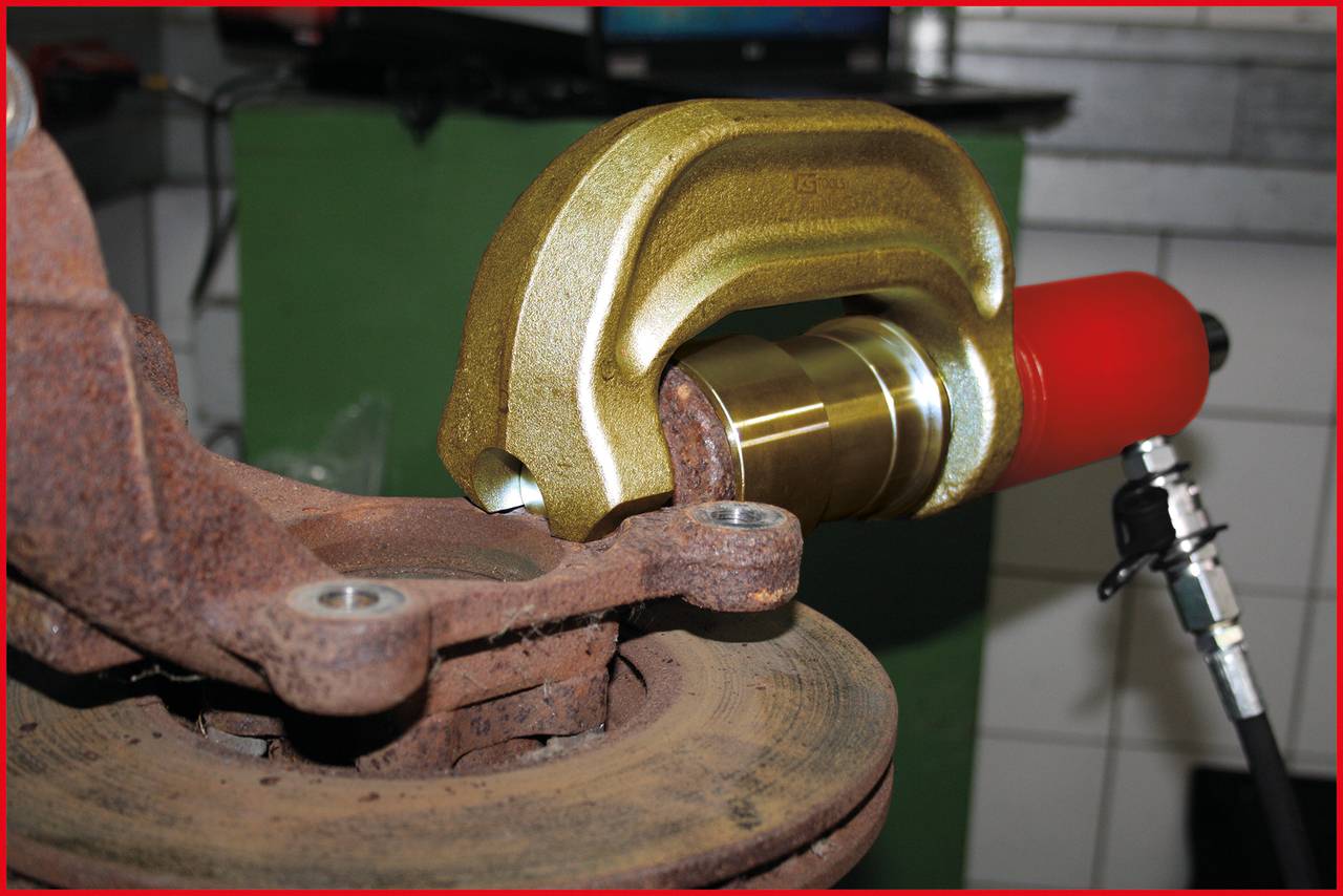 A specialised tool presses the bearing into the car's wheel suspension. It is used in a workshop.