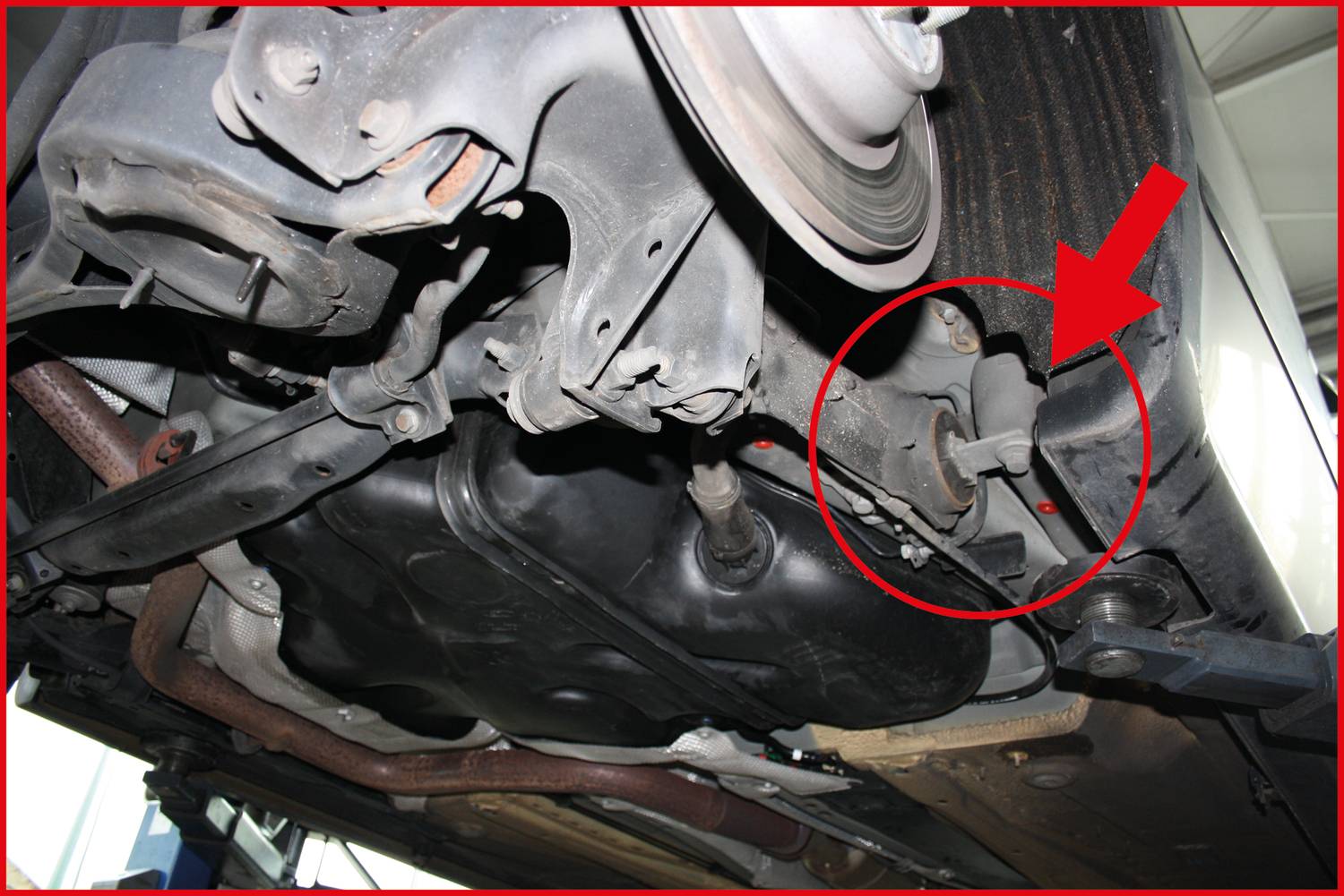 Vehicle underside with a highlighted area marked by a red circle and an arrow pointing to a specific vehicle component.