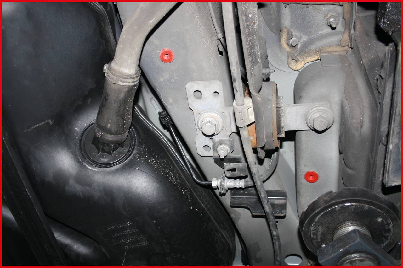 A vehicle underside with visible parts of the exhaust system and suspension. Various screws and fixings can be seen.