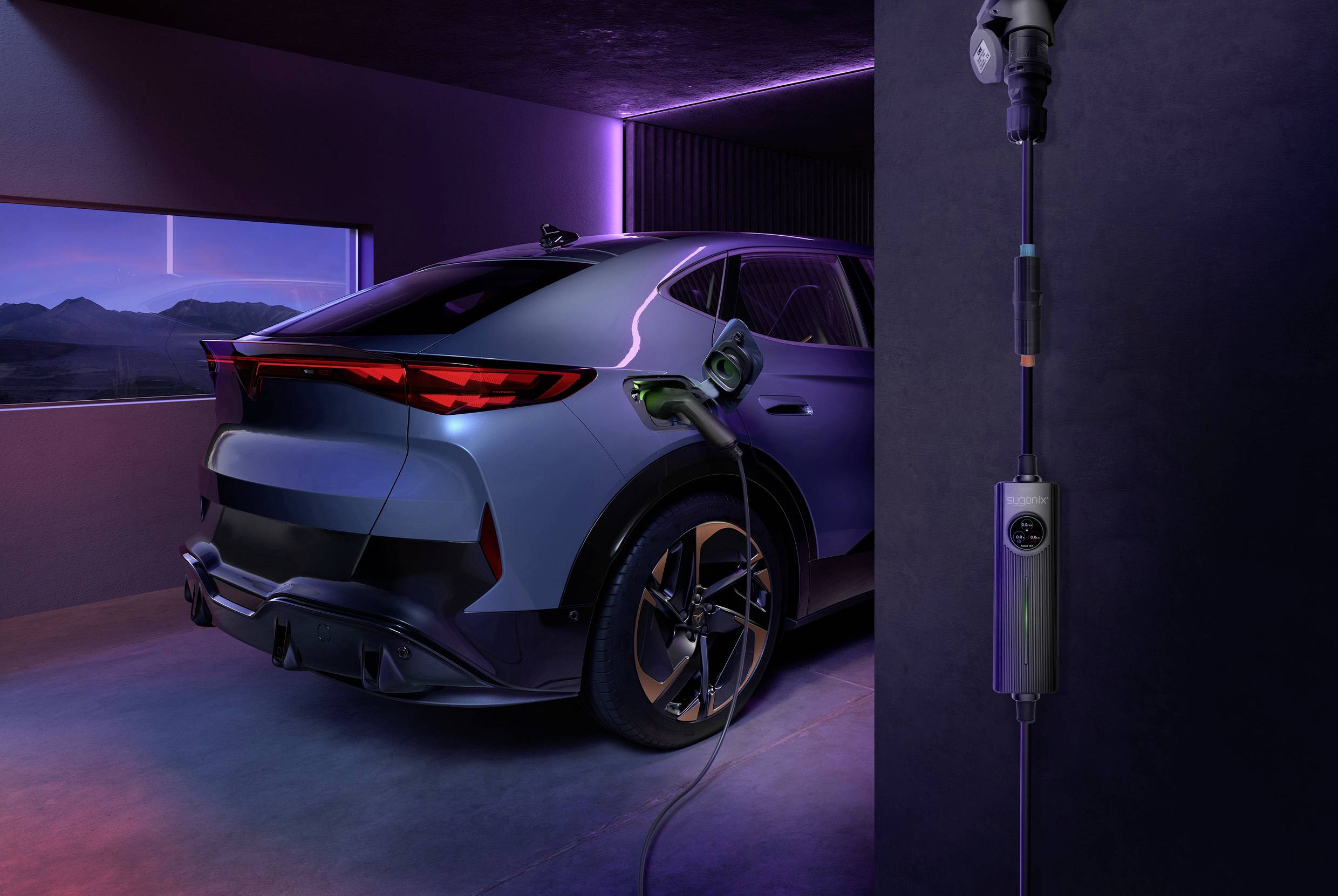 A silver electric car is charging in a modern garage. Mountains are visible through a window in the evening light in the background.