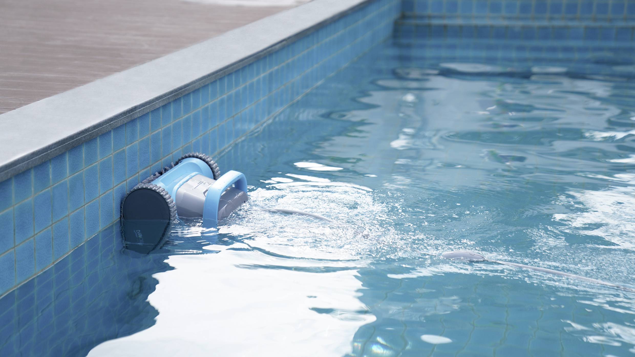 A pool robot is cleaning the blue tiled wall of a swimming pool. The water is moving gently around the device.
