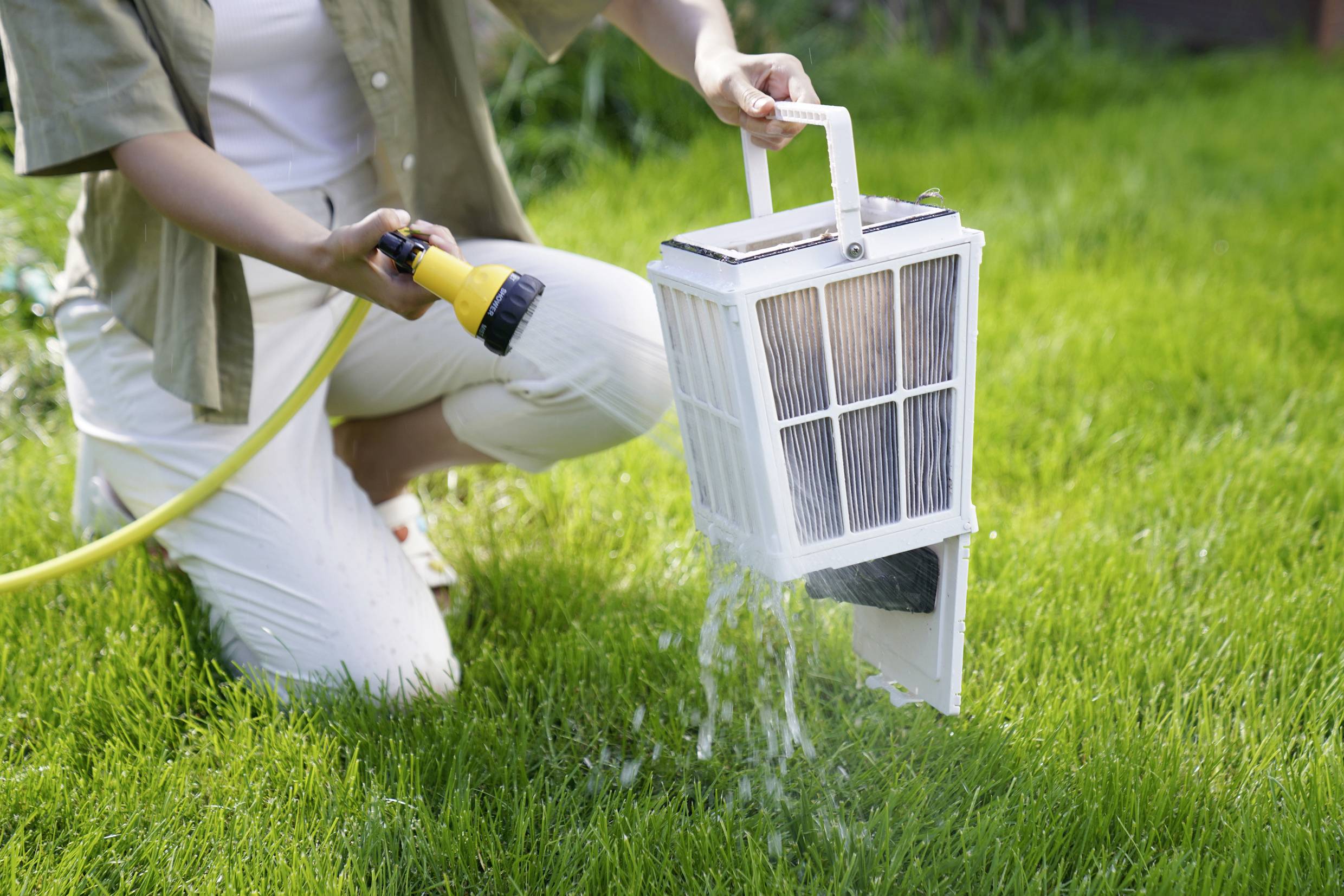 A person is cleaning a pool filter with a hosepipe over a green lawn.