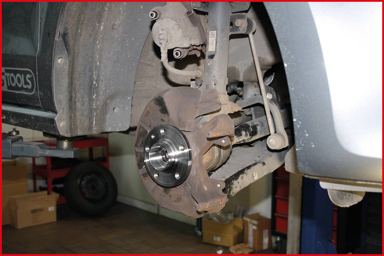 A car in a garage with an exposed brake disc on the front wheel, showing an ongoing repair or maintenance.