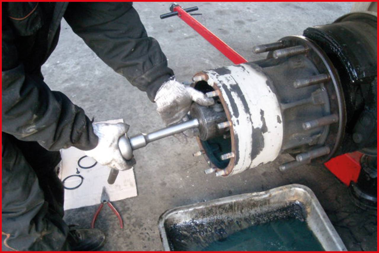 A person is repairing a mechanical component of a large vehicle. Hands are wearing gloves, and a tool is being used.