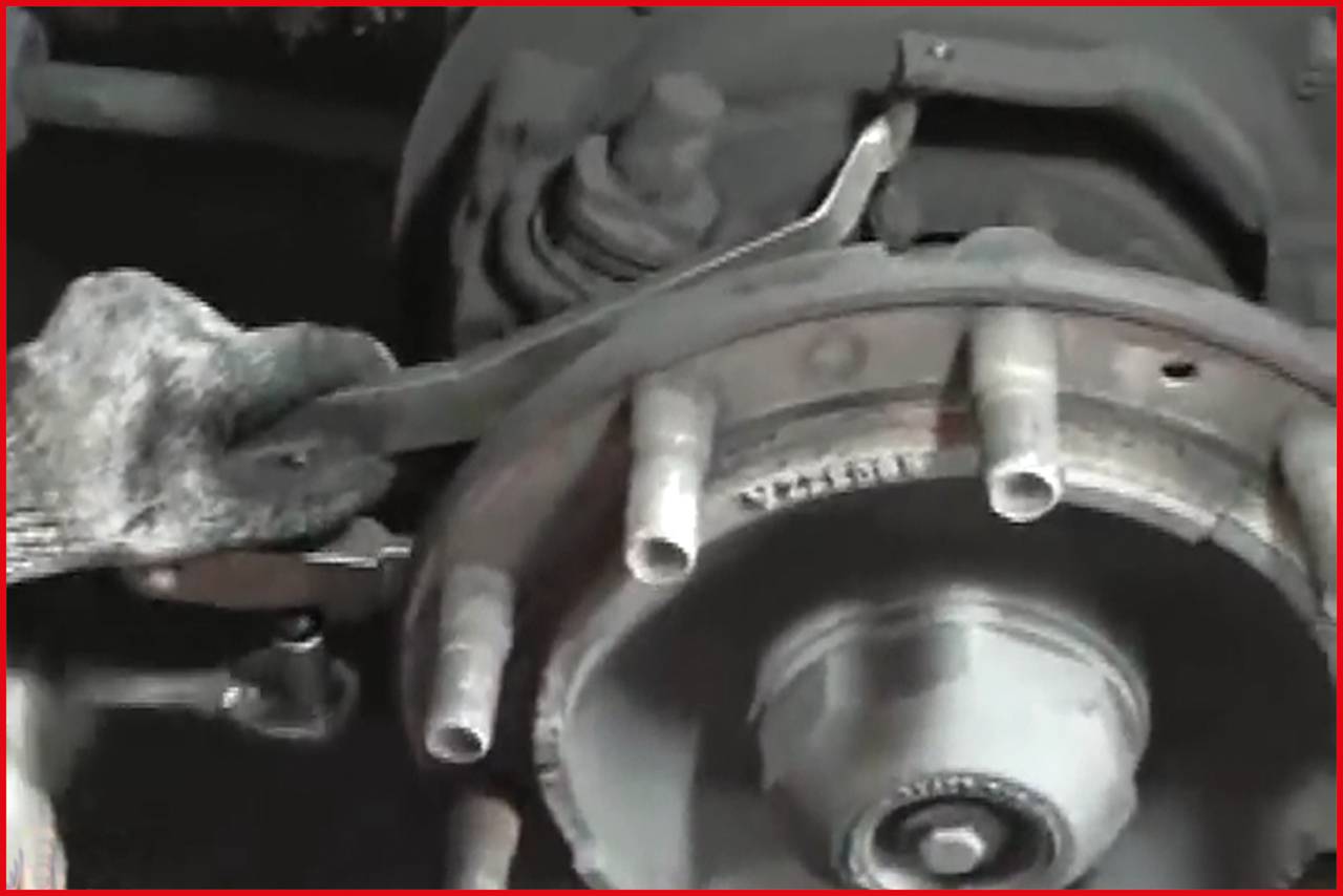 A gloved hand uses a tool to service a brake drum on a vehicle. The focus is on the repair process.