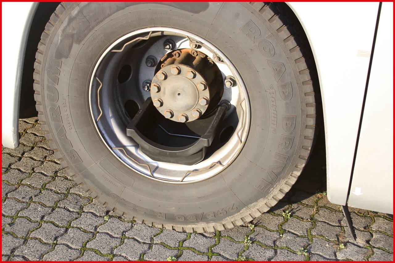 A bus tyre is seen close up. It is standing on a paved surface. The wheel nut and rim are visible.