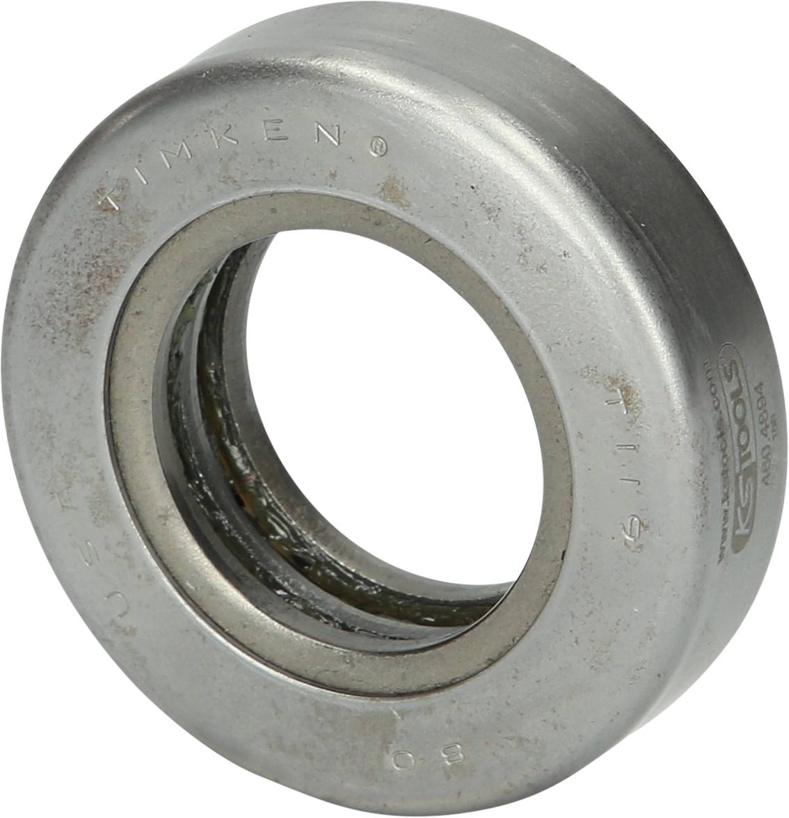 A silver rolling bearing lying on a light-coloured surface. The outer ring bears engraved markings and letters.