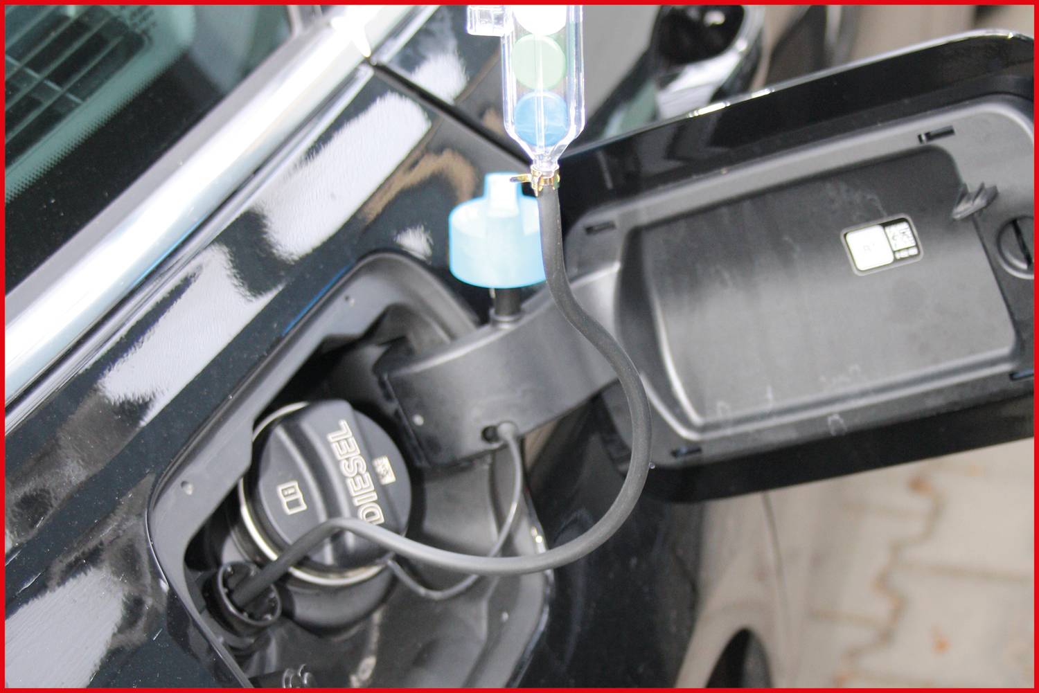Open fuel cap of a car with a diesel pump nozzle inserted. A measuring device is hanging at the opening.
