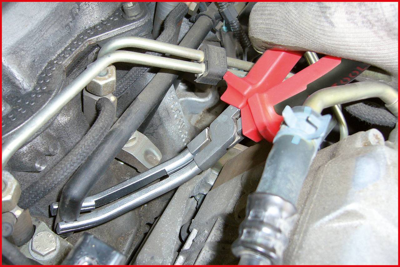 'A tool in a car's engine bay grasps a pipe. Another pipe is nearby. Hand in protective glove visible.'