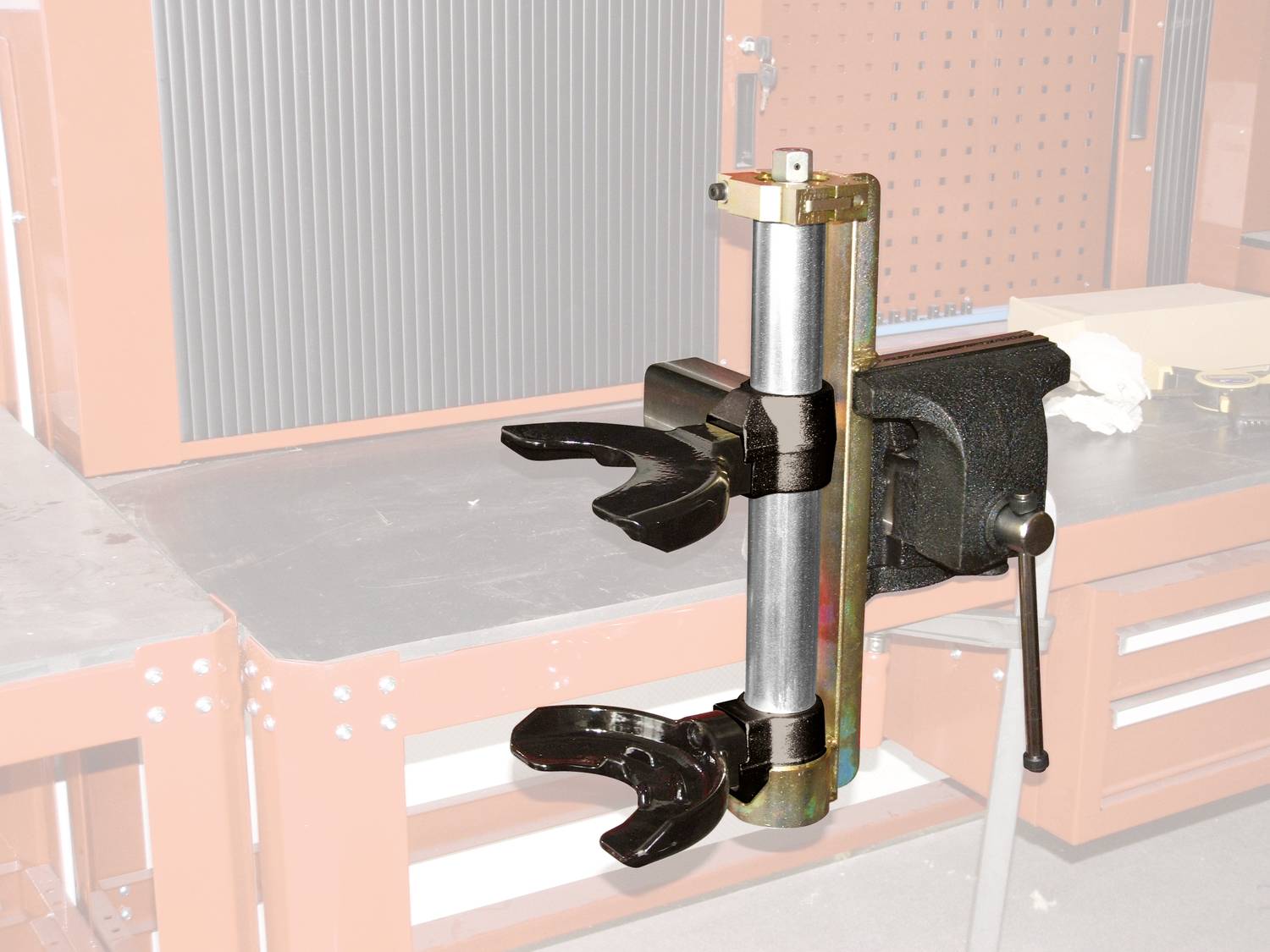 A metallic tool with two gripping arms is attached to a workbench. It is likely used for securing objects.