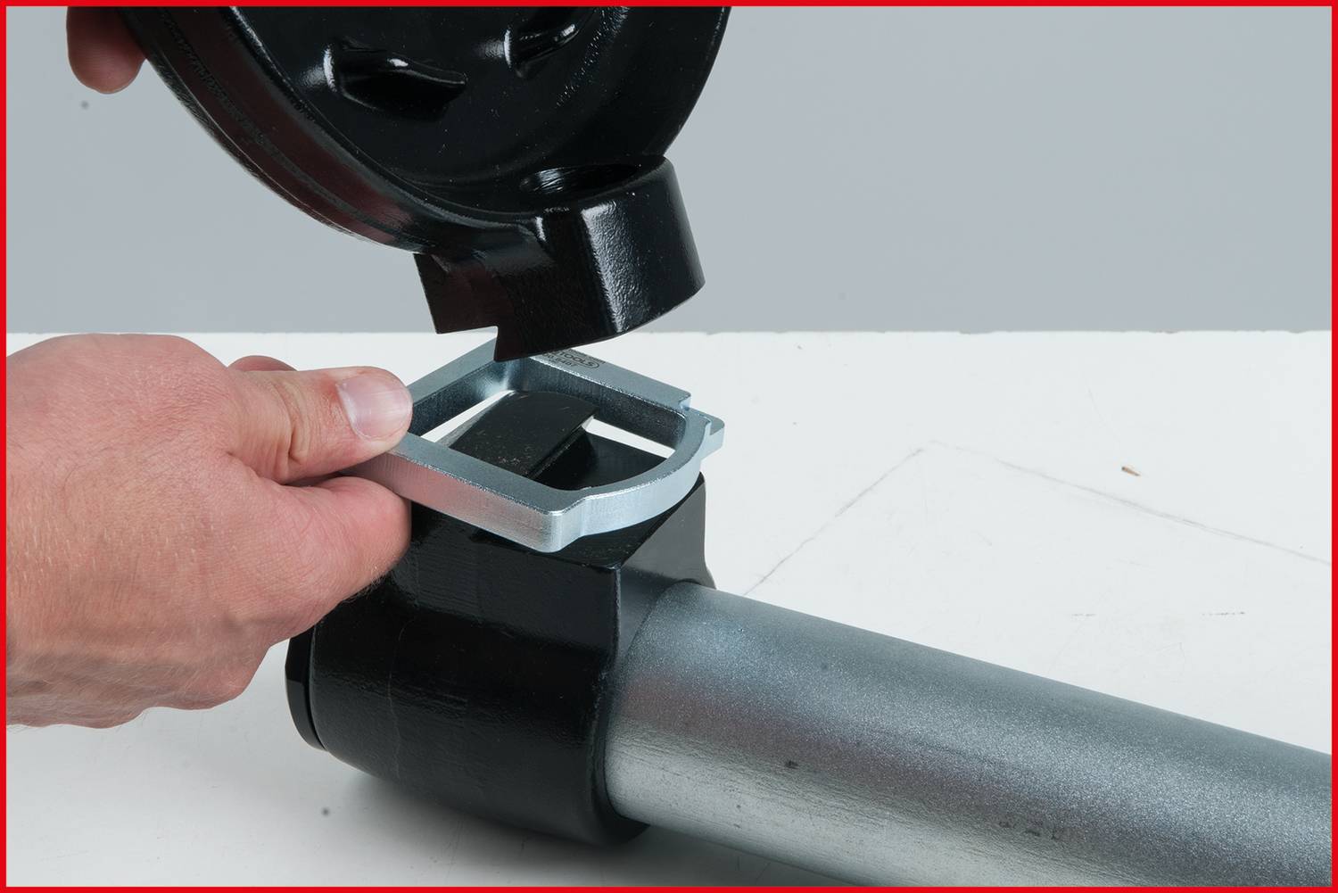 A person is installing a metal component onto a cylindrical pipe with a black cover and a square frame.