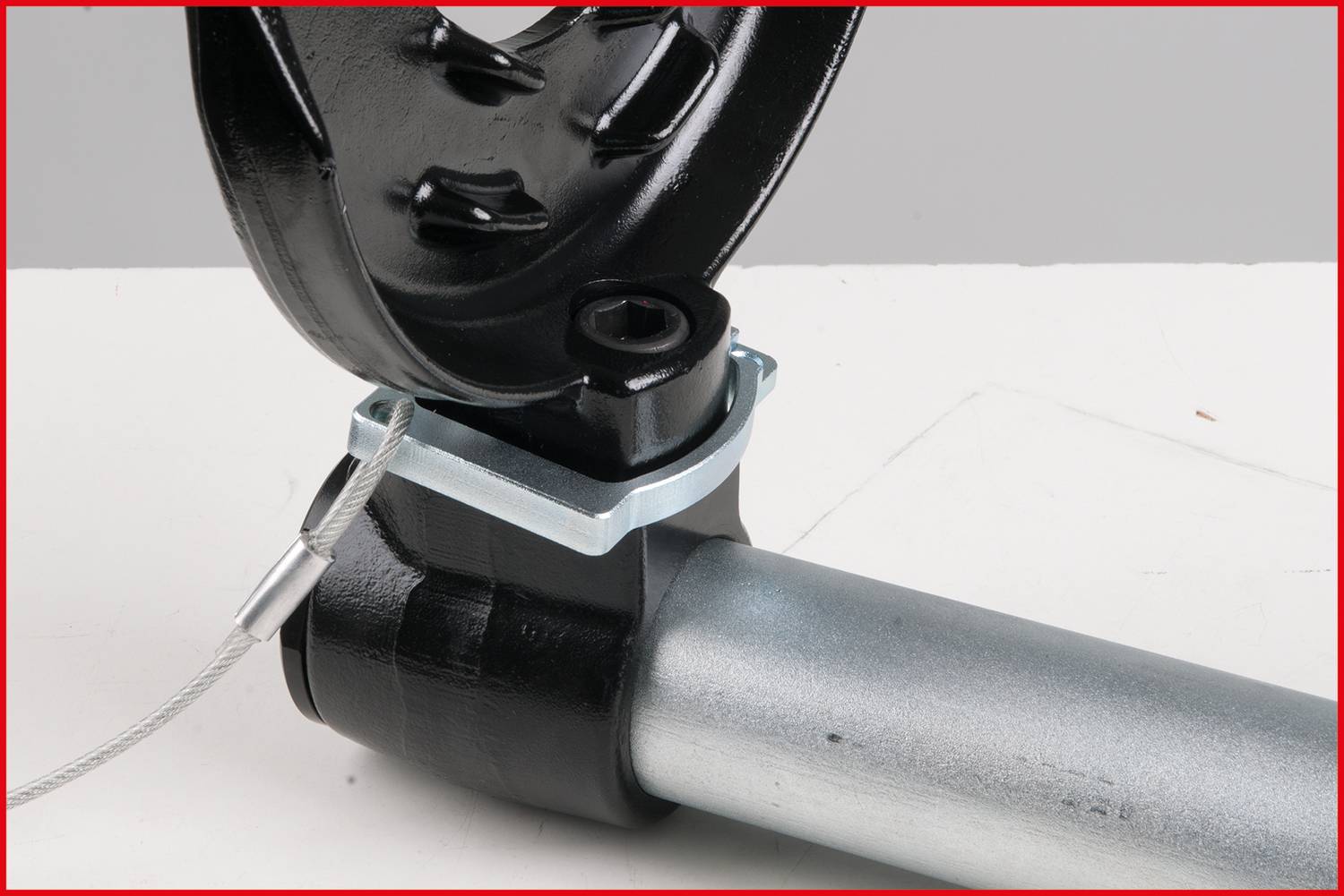 Close-up of a metallic connecting piece with black and silver paint finish, with a steel cable attached to it.