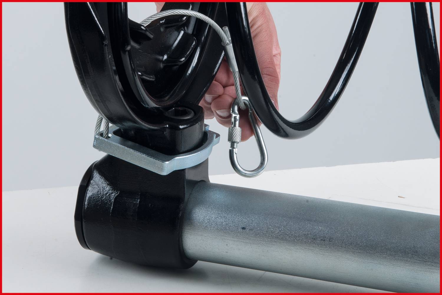 A hand is securing a metal clip to a pipe using a carabiner.