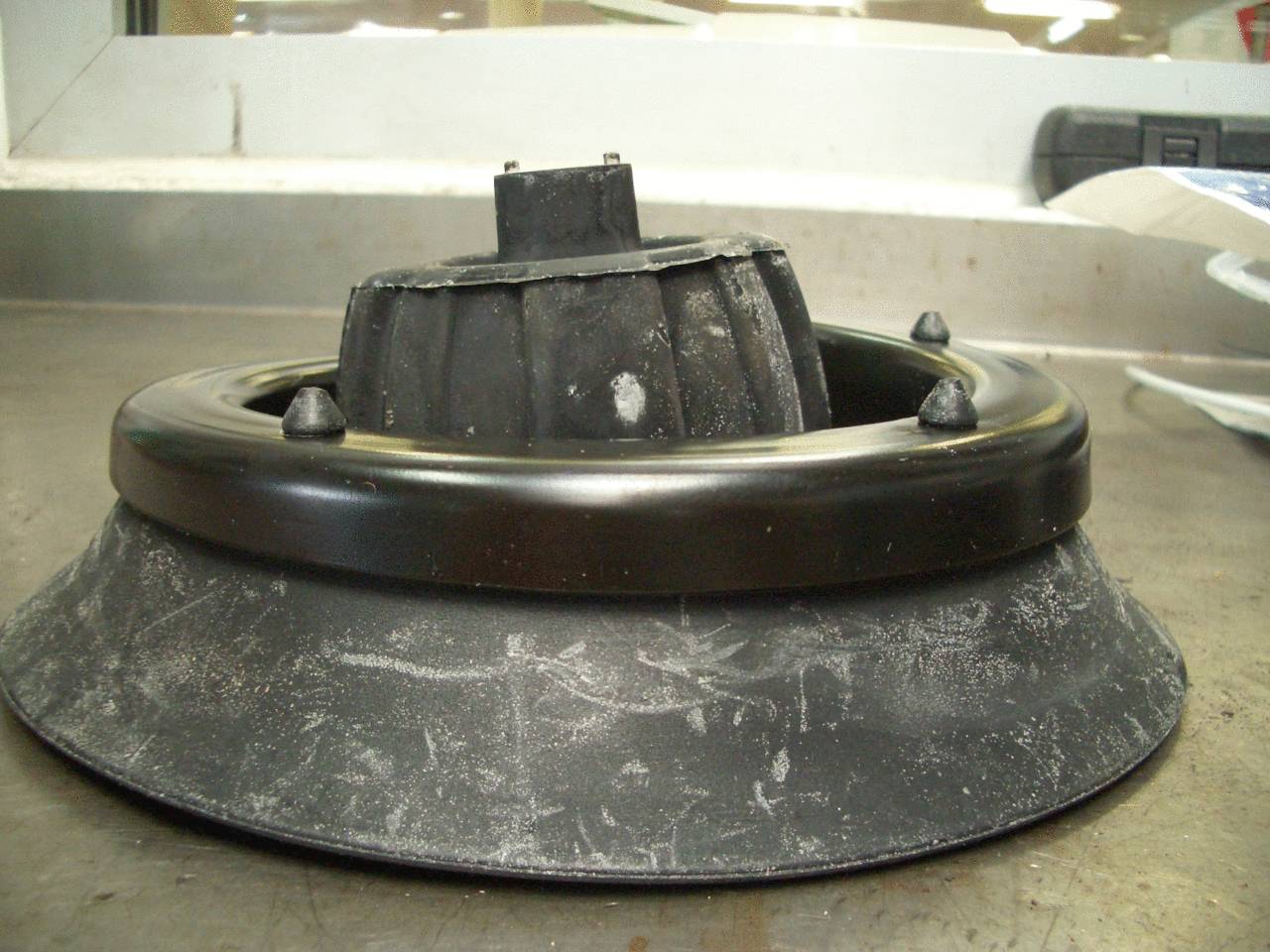 A black, round machine component made of metal and plastic sitting on a table. It appears well-used and shows signs of wear.