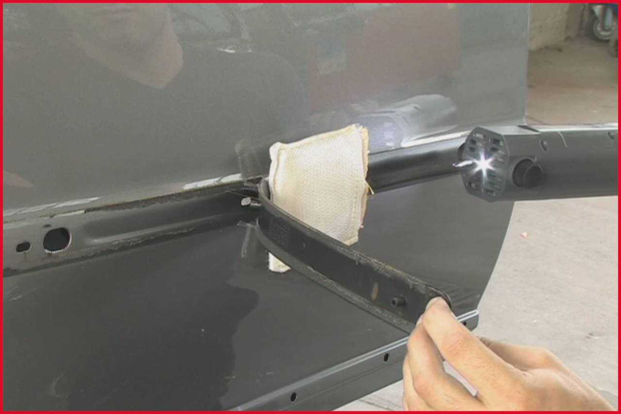'A tool worker repairs a dent on a car part with a machine that emits light, while a cloth serves as protection.'
