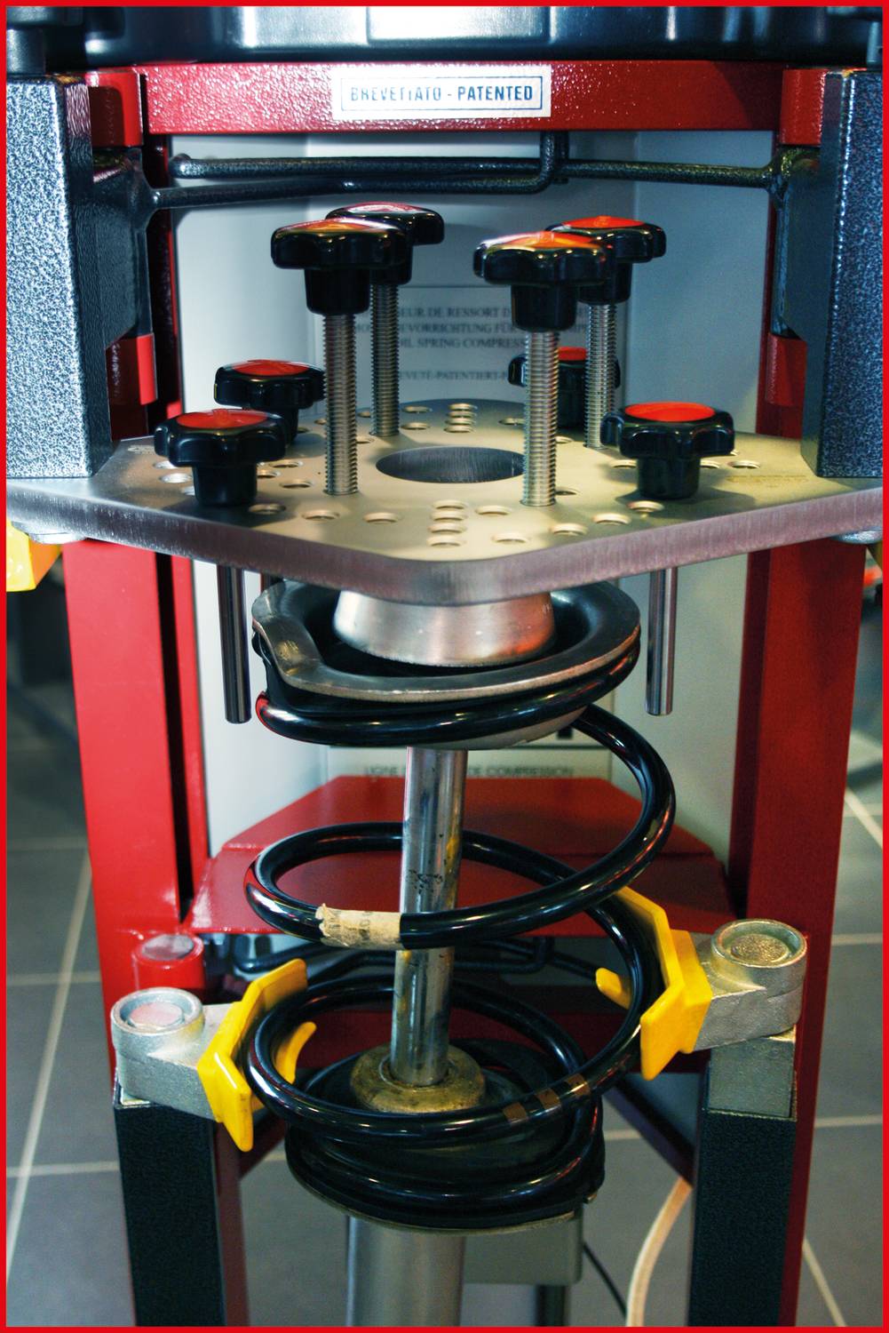 Device for adjusting and compressing springs with multiple adjustment knobs and an integrated spring system, in a workshop environment.