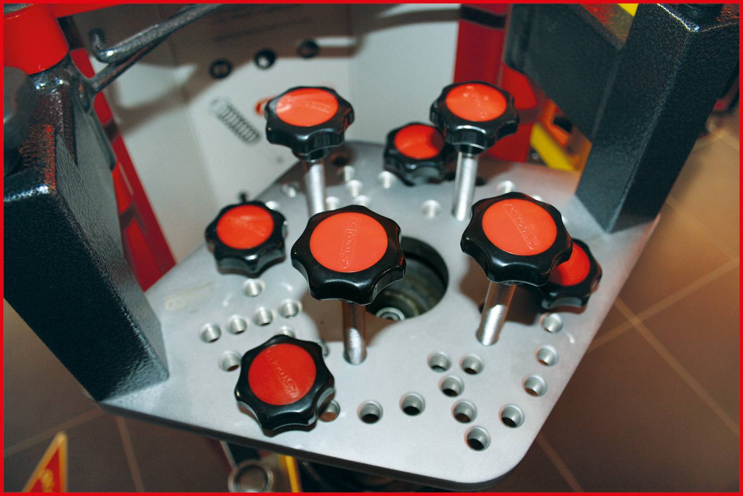 Machine with several red rotary knobs on a silver plate, likely for precision adjustments in a technical environment.