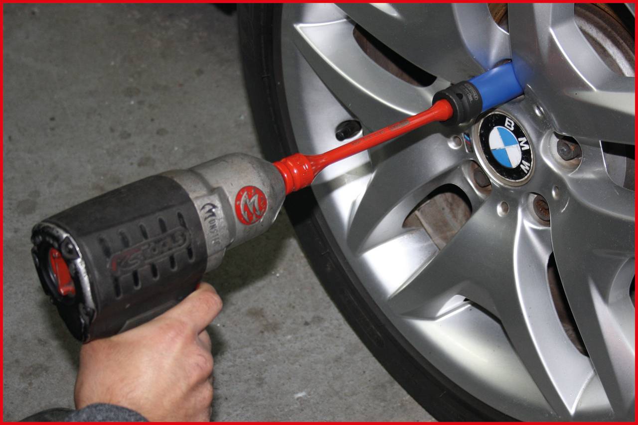 A person is tightening the wheel nuts of a car with an impact wrench. The car has silver rims.