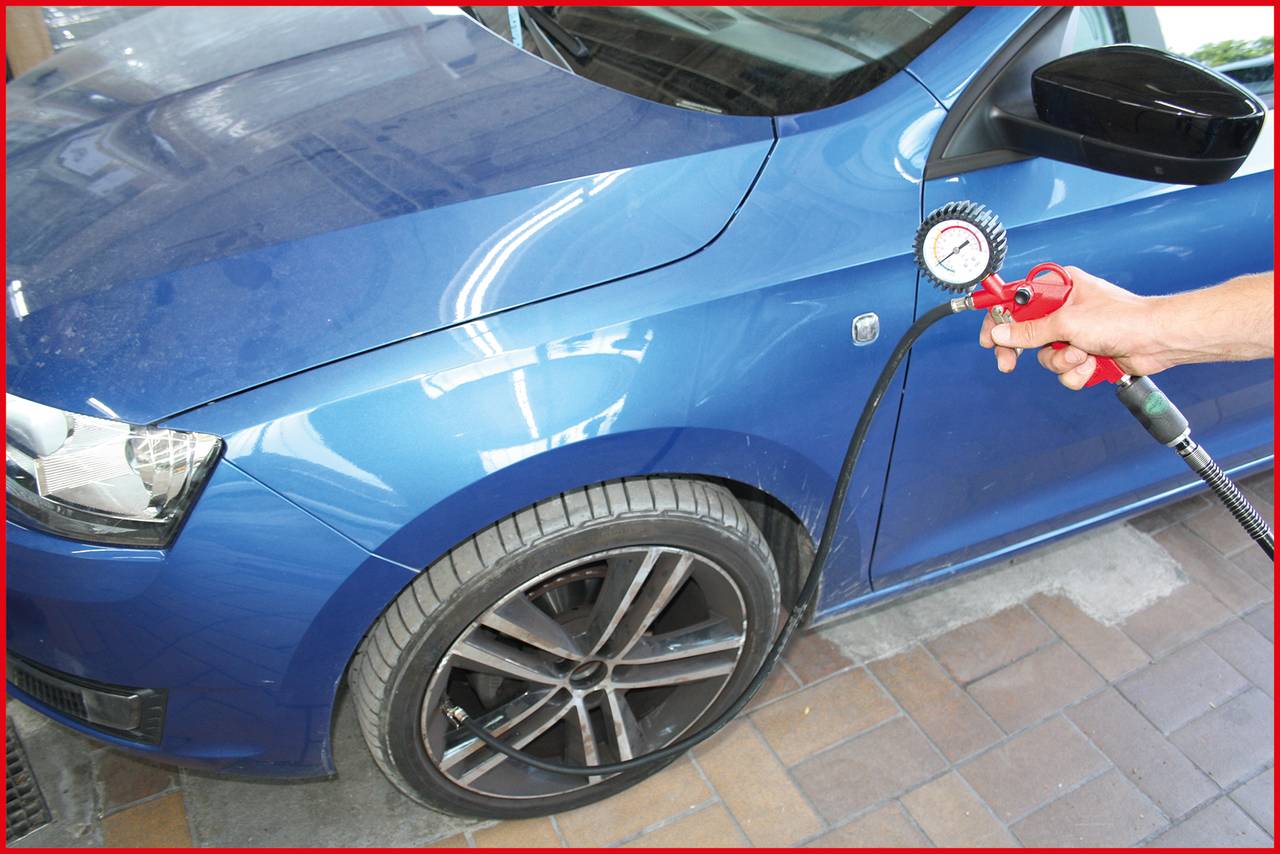 A blue car is being serviced, with air being pumped into the front tyre. A hand is holding a pressure gauge.