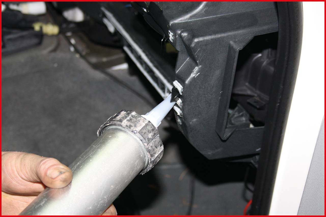 'A person is using a caulking gun to apply sealant to a vehicle surface.'