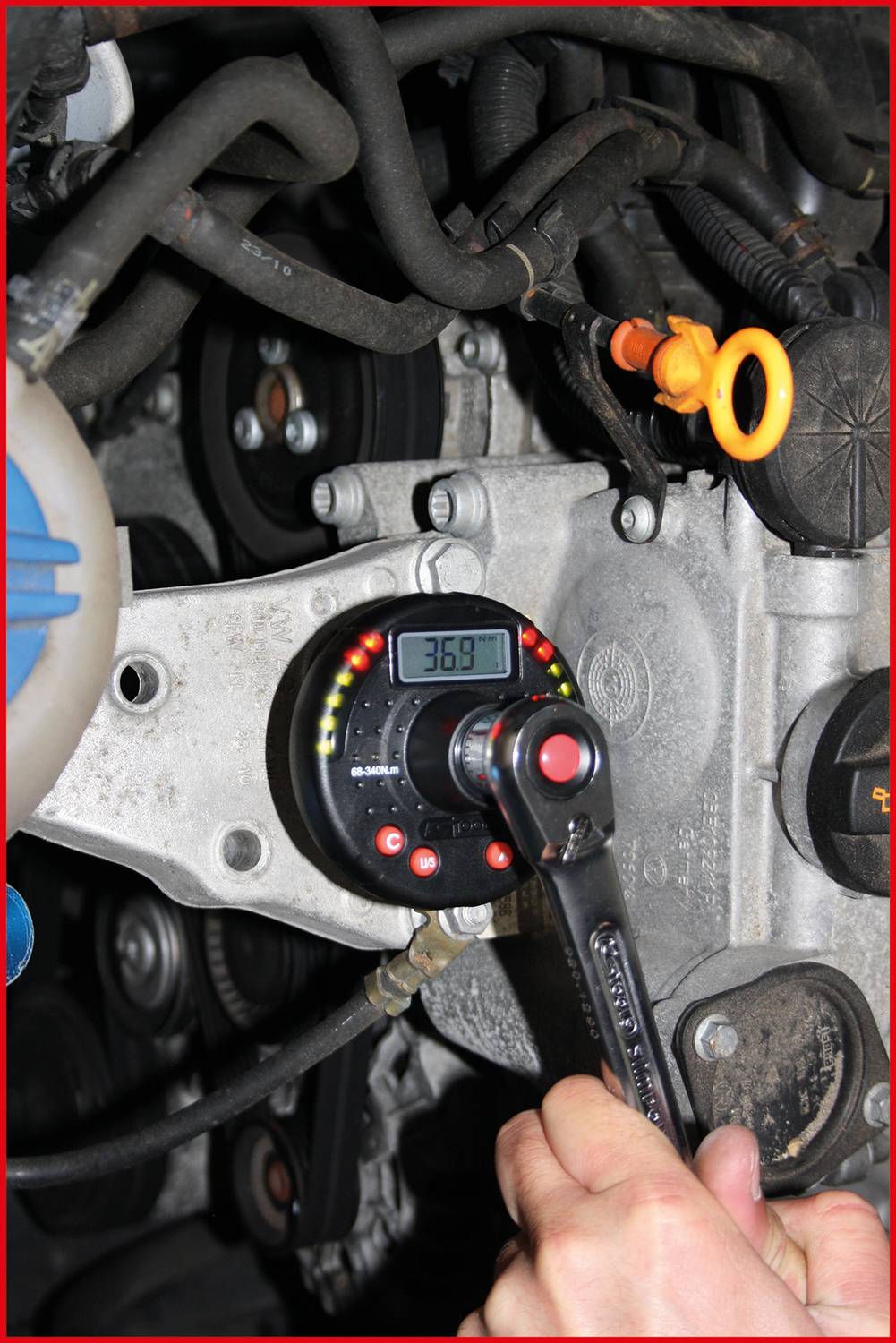 A hand is using a torque wrench to tighten a screw in a car engine bay. A digital display shows '36.8'.