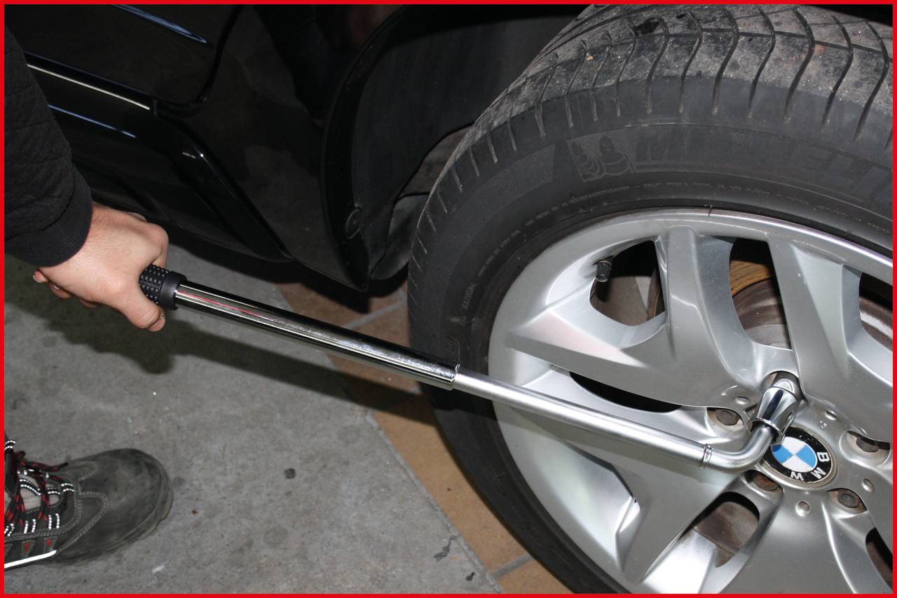 Close-up of a person tightening the wheel nuts of a car tyre with a torque wrench. The tyre is mounted on a silver rim.