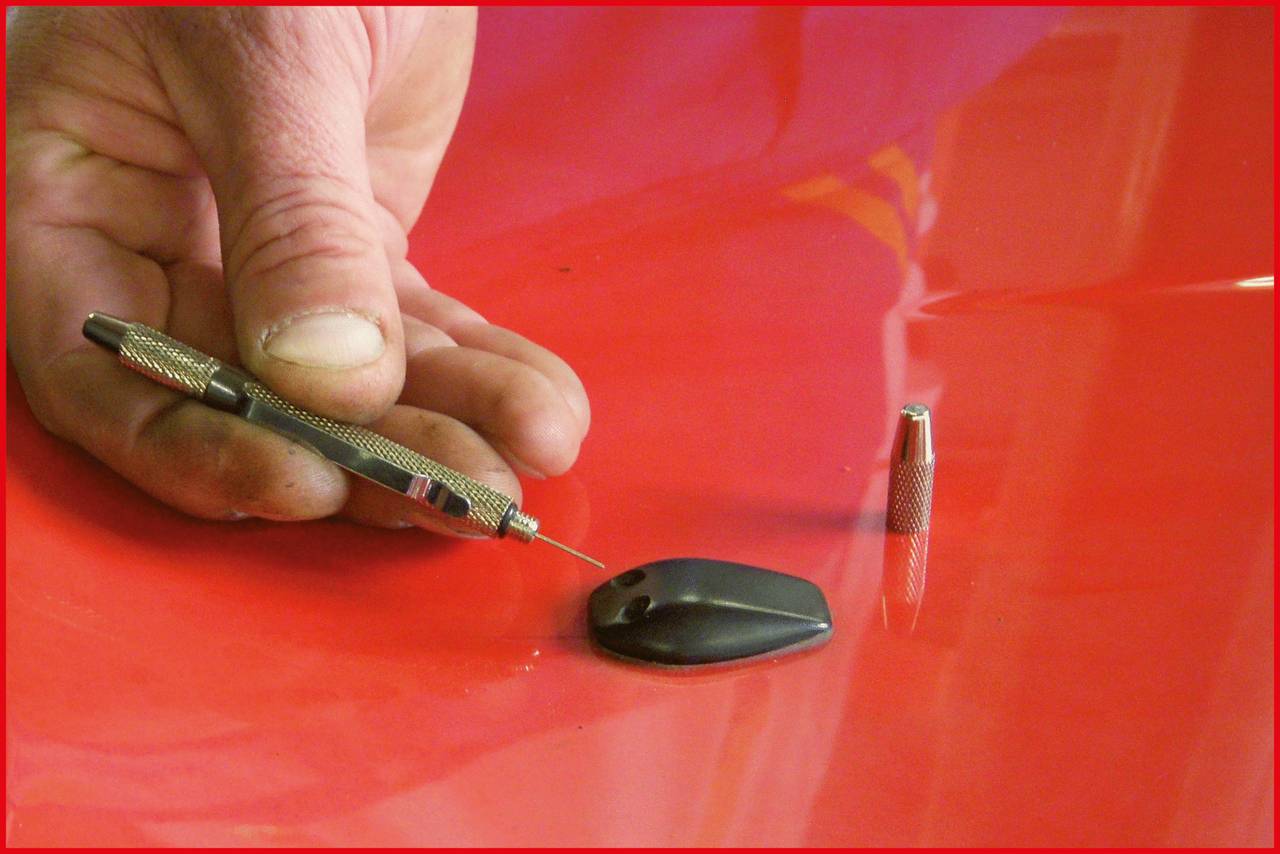 'Close-up of a hand holding a tool next to a black aerial on a red car roof.'
