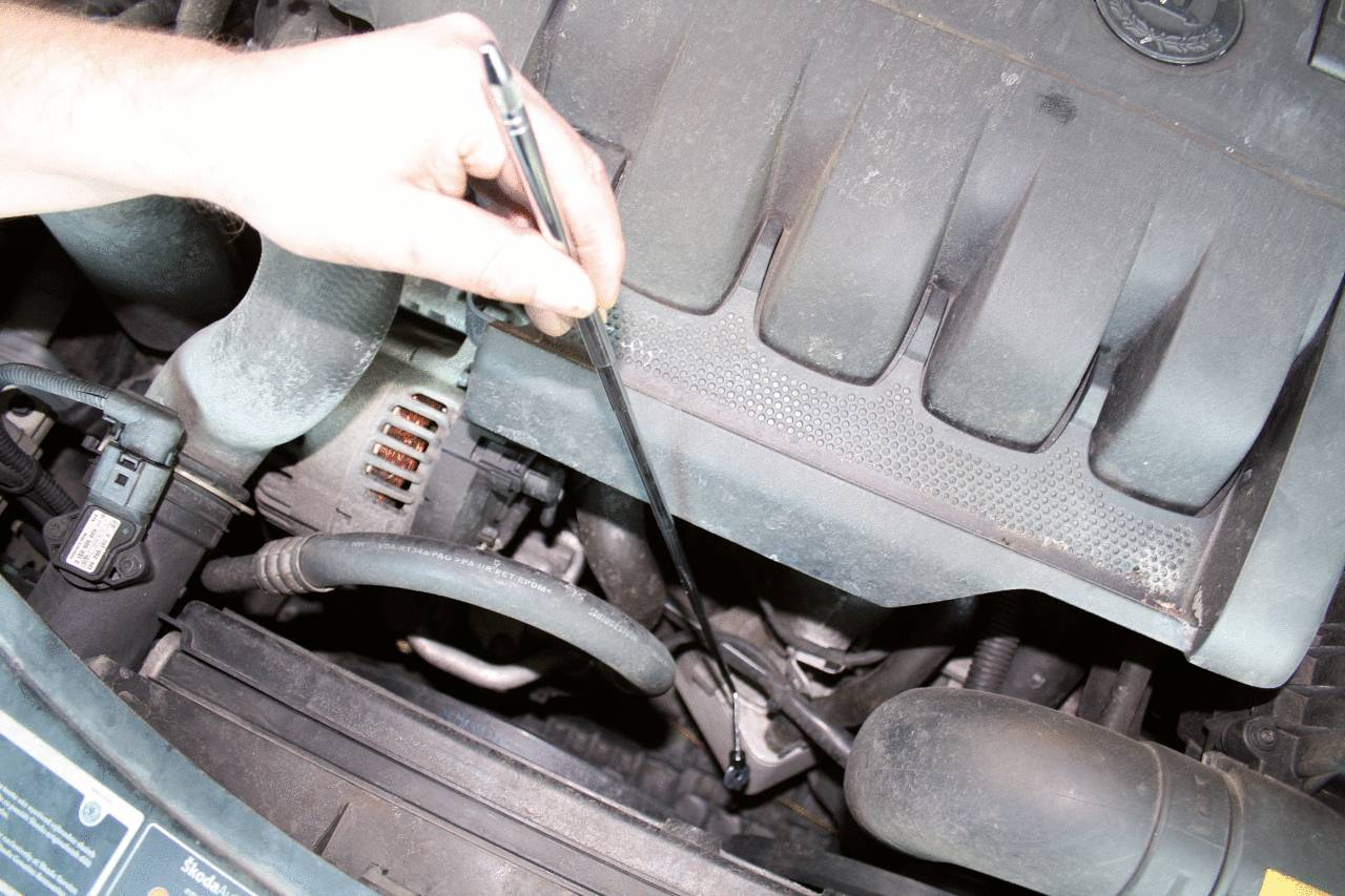 A hand holds an oil dipstick over a car radiator to check the oil level in the engine.